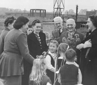 Kārlis Zariņš ar kundzi Henrietu (pirmā no labās) apmeklē ģimeņu hosteļa iemītniekus. Rietumvelsa, 1951. gada 19. maijs. Pēc ierašanās Lielbritānijā bēgļi tika izvietoti kopmītņu tipa nometnēs – hosteļos. Avots: Latvijas Ārlietu ministrijas arhīvs.